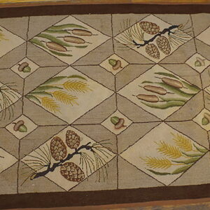 Brown and tan rug featuring a lattice design with pine cones, cattails, and wheat motifs on a wood floor.