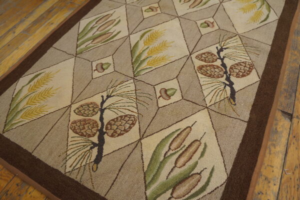 Beige and tan rug with a geometric grid pattern featuring pinecones, cattails, and wheat on a distressed wooden floor.