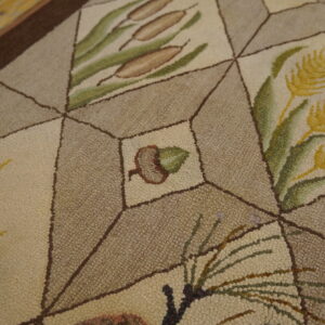 Close-up of a loop pile rug with a geometric pattern, featuring botanical motifs like acorns and cattails.