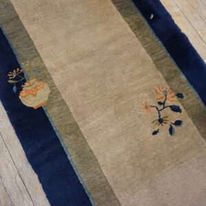 Beige runner rug with navy and olive stripes and sparse floral accents rests on weathered wood planks.