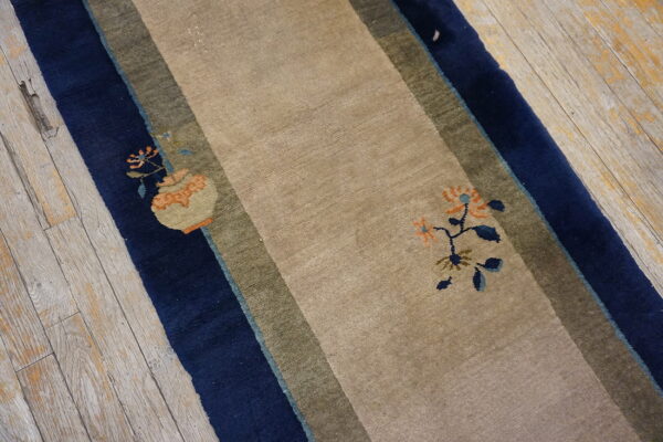 Beige runner rug with navy and olive stripes and sparse floral accents rests on weathered wood planks.
