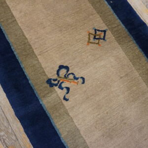 Tan runner rug with navy and olive stripes, abstract motifs, lying on distressed gray wood flooring.