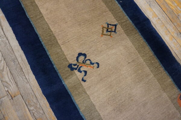 Tan runner rug with navy and olive stripes, abstract motifs, lying on distressed gray wood flooring.