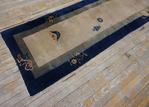 Runner rug featuring a tan field, navy border, and small orange and blue decorative motifs on wood flooring.