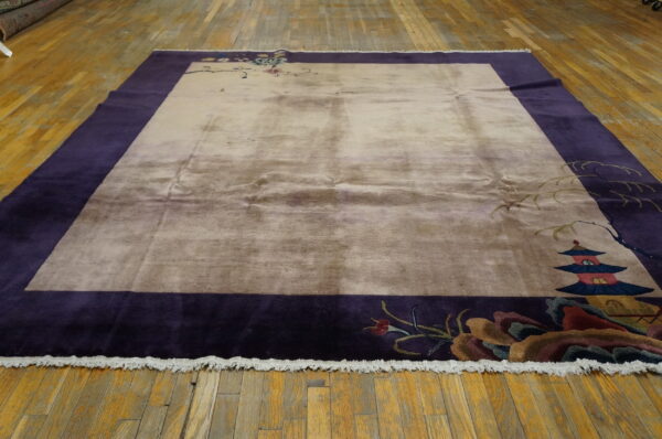 Beige and purple rectangular rug with asian pagoda and floral motifs lying on rustic wood floorboards.