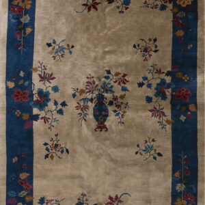 Tan rug featuring a floral vase motif, scattered sprigs, and a wide indigo border with complementing flowers.