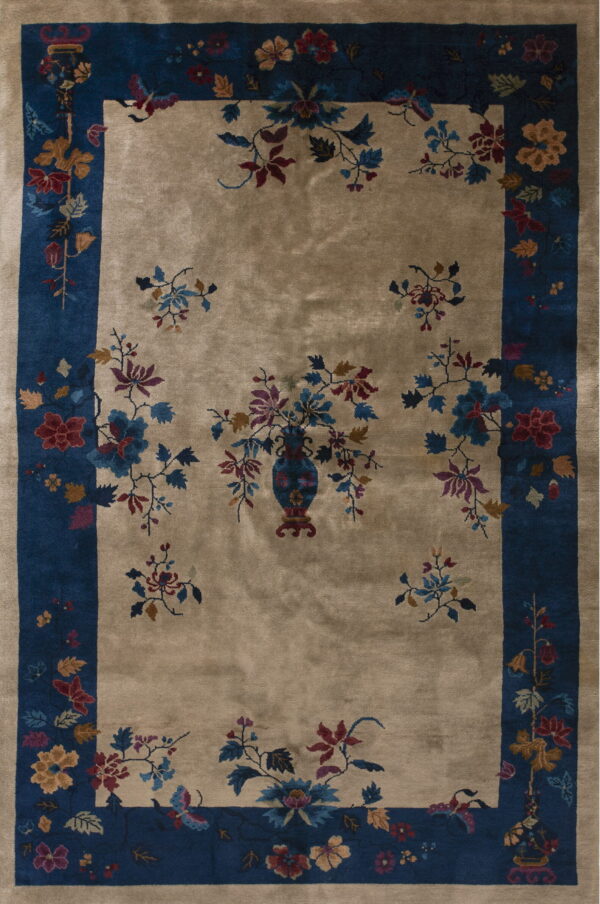 Tan rug featuring a floral vase motif, scattered sprigs, and a wide indigo border with complementing flowers.