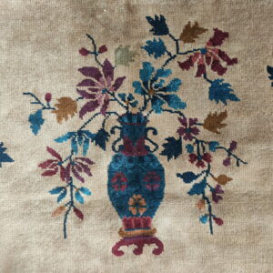 Low-pile rug detail showing a blue vase with multicolored flowers against a beige background.