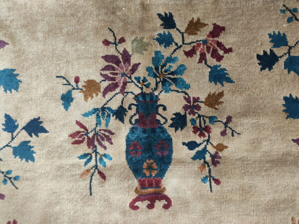 Low-pile rug detail showing a blue vase with multicolored flowers against a beige background.