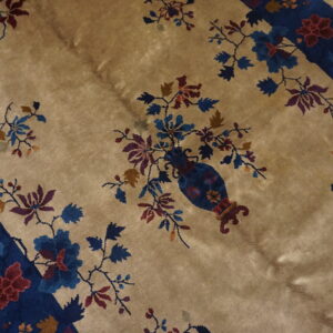 Tan rug detail showing a blue vase with colorful flowering branches and a wide indigo border.