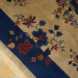 Tan and navy rug with multicolor floral and vine patterns shown closely on distressed wood flooring.