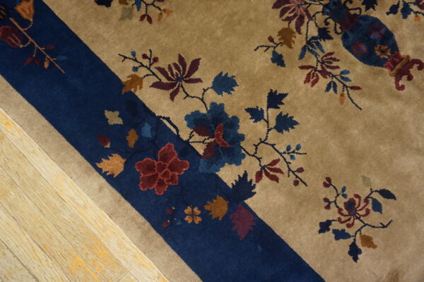 Tan and navy rug with multicolor floral and vine patterns shown closely on distressed wood flooring.