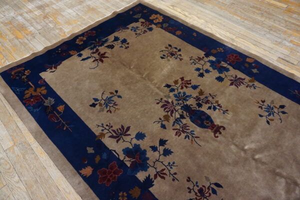 Low-pile beige rug with a wide navy blue floral border rests on distressed wood plank flooring.