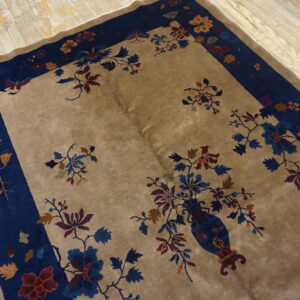Beige rug with deep blue border displays a central floral vase design on weathered wood planks.