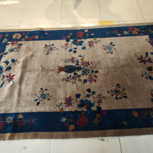 Beige rug with a central vase motif and blue border covered in dense, multicolored flowers.