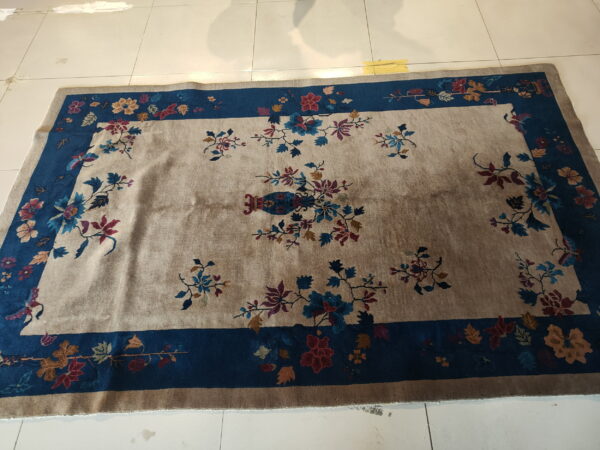 Beige rug with a central vase motif and blue border covered in dense, multicolored flowers.