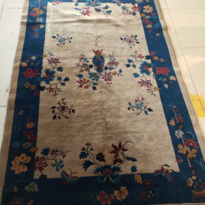 A beige and blue floral rug with a central vase motif sits on a white tiled floor.