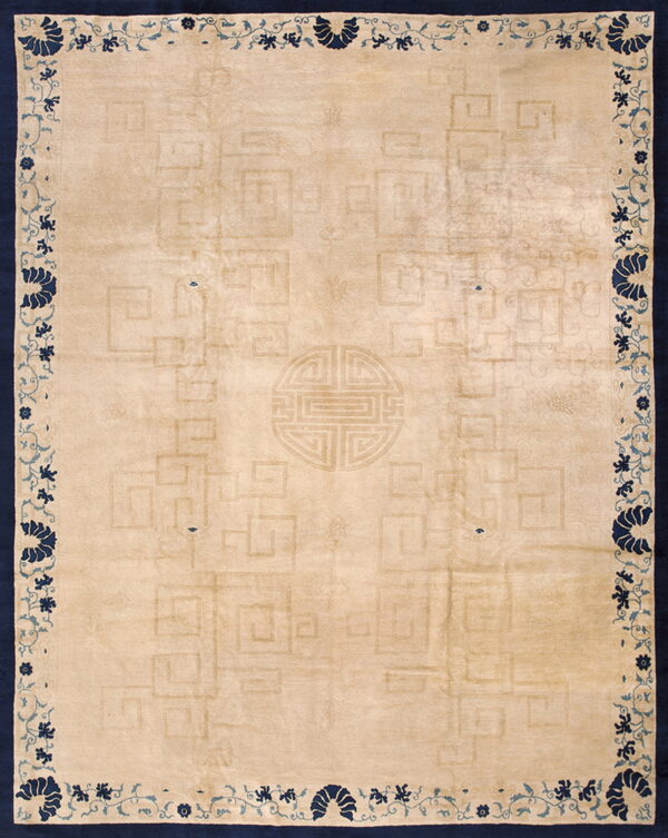 Tan rug featuring a low-contrast geometric pattern, framed by a dark blue border with vine and floral motifs.