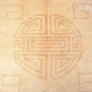 Tan rug with a large, low-contrast geometric key pattern and faint overall field texture.