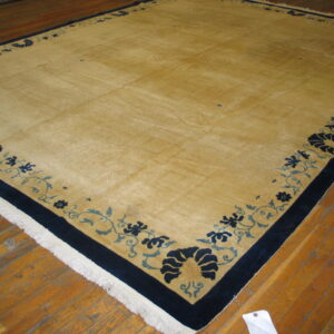 Large gold rug with a wide navy and blue floral border resting on worn wooden floors.