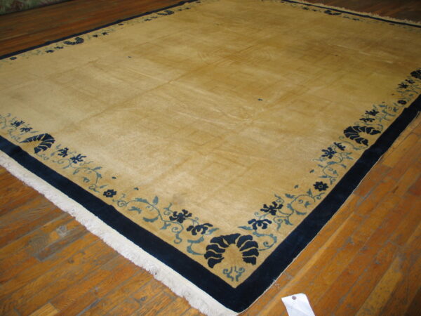 Large gold rug with a wide navy and blue floral border resting on worn wooden floors.