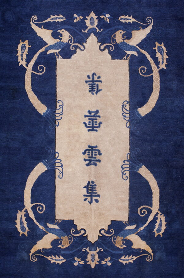 Blue rug with a rectangular beige cartouche containing characters, surrounded by stylized tan animal and vine motifs.