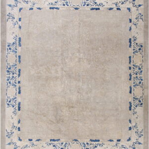Muted beige rug featuring a tone-on-tone design and a high-contrast border with bold blue foliage.