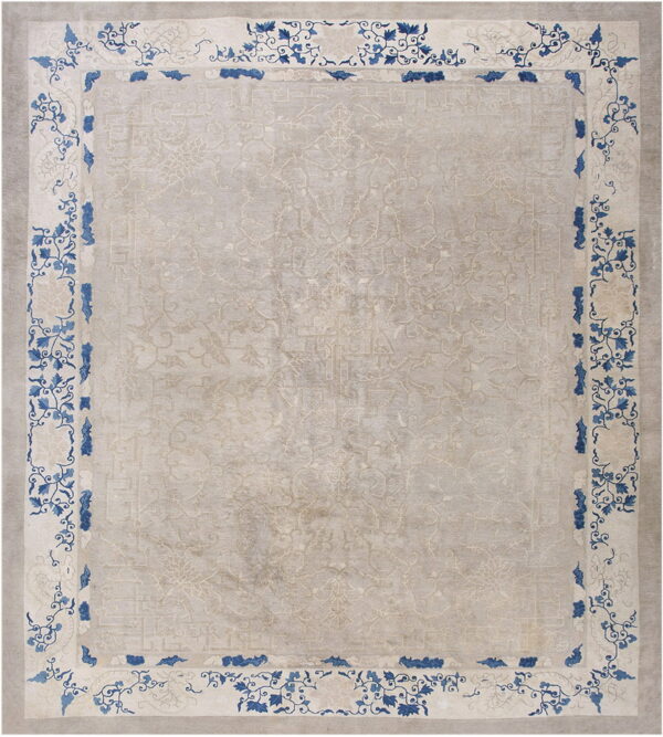 Muted beige rug featuring a tone-on-tone design and a high-contrast border with bold blue foliage.