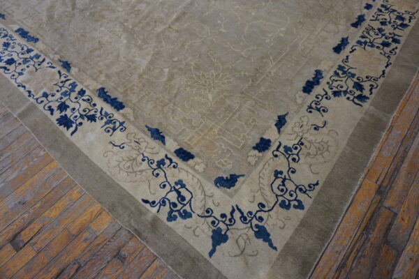 Beige low-pile rug with a blue floral border resting on distressed wood plank flooring.