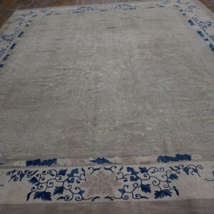 Light gray plush rug with a dark blue floral border laid out on brown wooden plank flooring.