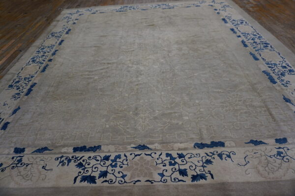 Light gray plush rug with a dark blue floral border laid out on brown wooden plank flooring.