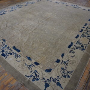 Beige area rug with subtle field patterns and a bold indigo floral border rests on wood planks.