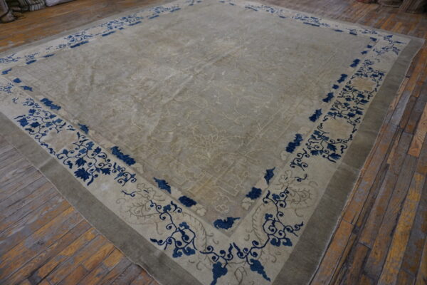 Beige area rug with subtle field patterns and a bold indigo floral border rests on wood planks.