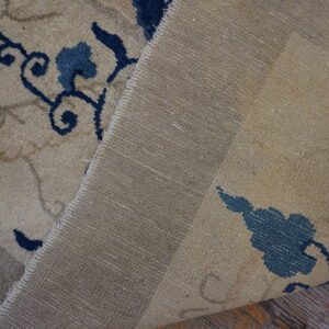 Beige patterned rug is folded back, showing its blue design, coarse backing, and wood flooring.