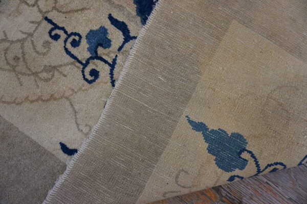 Beige patterned rug is folded back, showing its blue design, coarse backing, and wood flooring.