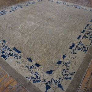 A large low-pile beige rug featuring blue floral borders rests on rustic wooden plank flooring.