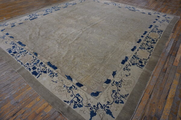 A large low-pile beige rug featuring blue floral borders rests on rustic wooden plank flooring.