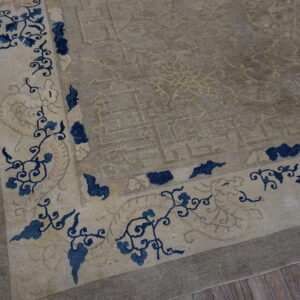 A taupe rug corner with low pile features a light border band with navy blue floral designs on wood flooring.
