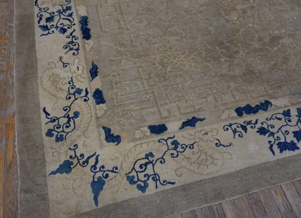 A taupe rug corner with low pile features a light border band with navy blue floral designs on wood flooring.
