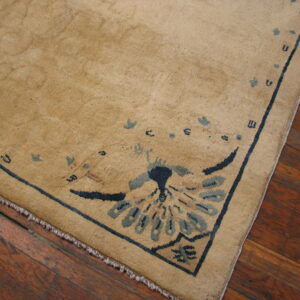 Low-pile tan rug featuring navy blue and slate motifs, placed on dark hardwood flooring.
