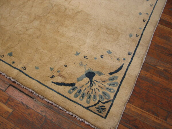 Low-pile tan rug featuring navy blue and slate motifs, placed on dark hardwood flooring.