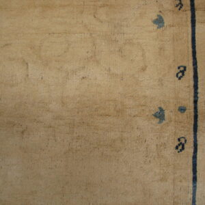 Tan low-pile rug on wood floor showing a thick dark blue vertical line and scattered motifs.