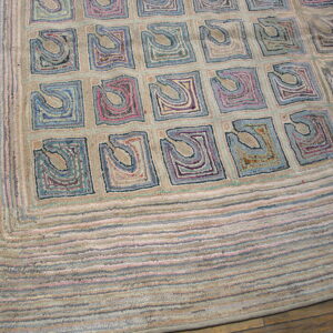 Beige hooked rug with a grid of abstract squares in blue, purple, and dusty rose colors on a wood floor.
