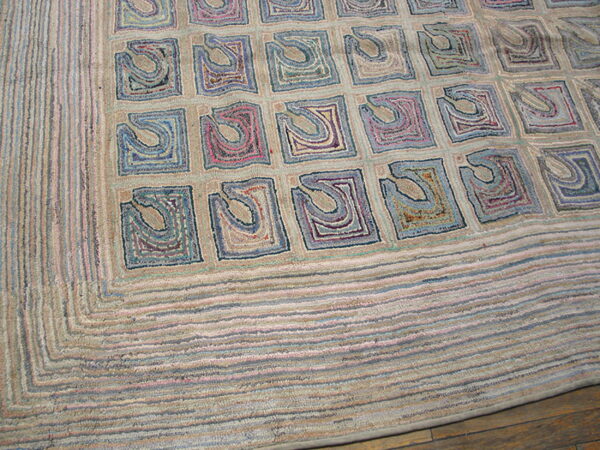 Beige hooked rug with a grid of abstract squares in blue, purple, and dusty rose colors on a wood floor.