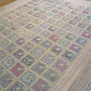 A heavily textured low-pile rug features colorful squares and looping motifs on a light beige background over wood floor.