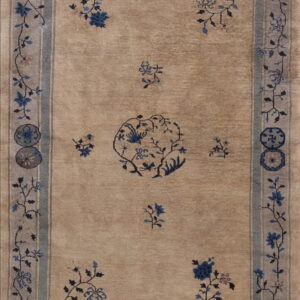 Muted tan rug displaying blue floral motifs, a central vine pattern, and gray-blue striped borders.