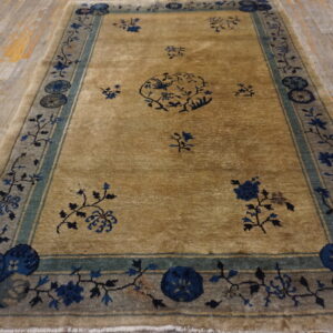 Tan rug with scattered blue floral pattern and a wide gray-blue border on light wood planks.