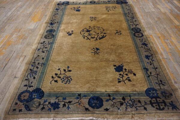 Tan rug with scattered blue floral pattern and a wide gray-blue border on light wood planks.