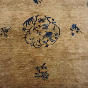 A tan rug with a plush pile features a dark blue floral and bird medallion and a slate blue striped border.
