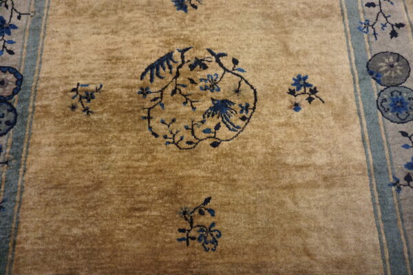 A tan rug with a plush pile features a dark blue floral and bird medallion and a slate blue striped border.